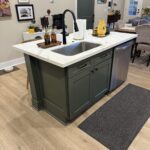 Kitchen island with cabinets painted dark green, white quartz countertop, and matte black faucet, from a cabinet painting job in Greenville, SC