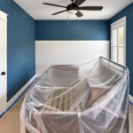 Bedroom with deep blue painted walls, white shiplap accent wall and white trim, with furniture covered in plastic during an interior painting project in Greenville, SC